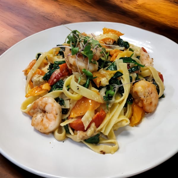 Shrimp pasta with fettuccine, spinach, bell peppers, and microgreens on a white plate.