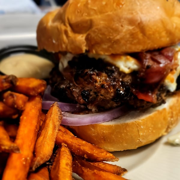A Digger's Ales N' Eats burger with bacon, cheese, and red onion, served with sweet potato fries.