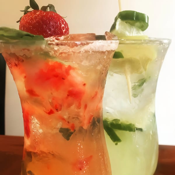 Two refreshing cocktails, one strawberry and one lime, garnished with fresh fruit and herbs.