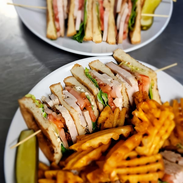 Two plates of Digger's Ales N' Eats club sandwiches with waffle fries and pickles.