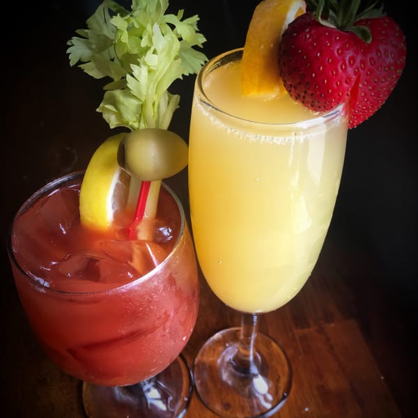 A Bloody Mary garnished with celery and olive, next to a Mimosa with orange and strawberry.