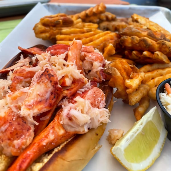 A Digger's Ales N' Eats lobster roll with waffle fries, coleslaw, and a lemon wedge.