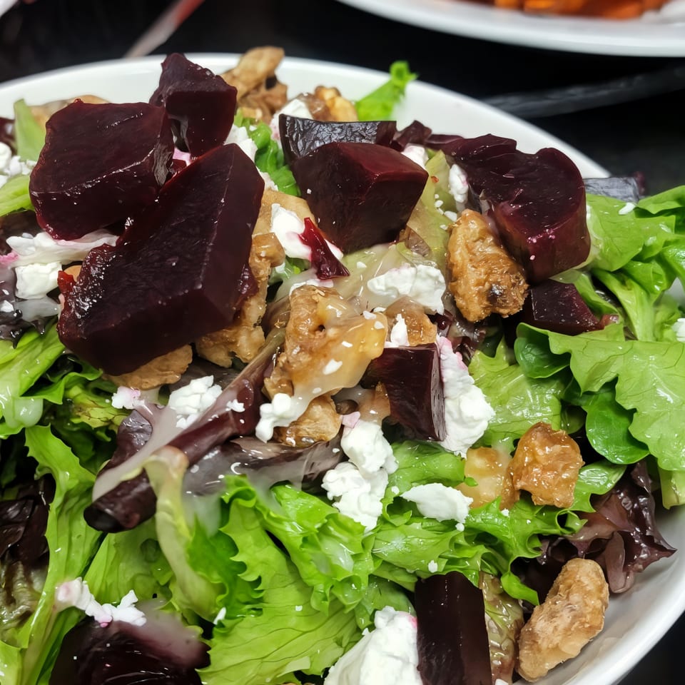 Close-up of a vibrant salad with green and red lettuce, beets, walnuts, and feta cheese.