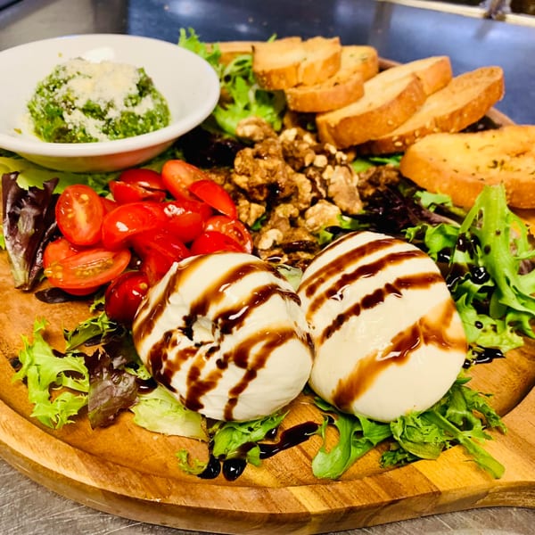 A Digger's Ales N' Eats appetizer board with burrata, pesto, tomatoes, walnuts, and toasted bread.
