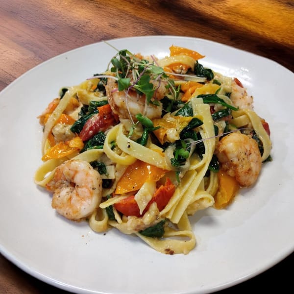 Shrimp fettuccine pasta with spinach, bell peppers, and microgreens on a white plate.